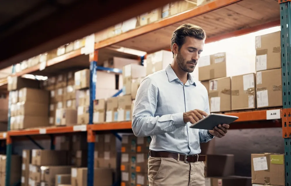 Logistics manager conducting inventory checks using an iPad within a well-organized warehouse, demonstrating efficient digital management in the supply chain.