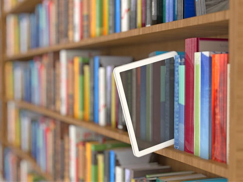 An iPad nestled between books on a shelf, symbolizing the blend of traditional education with modern digital learning tools available for schools at iPadify.