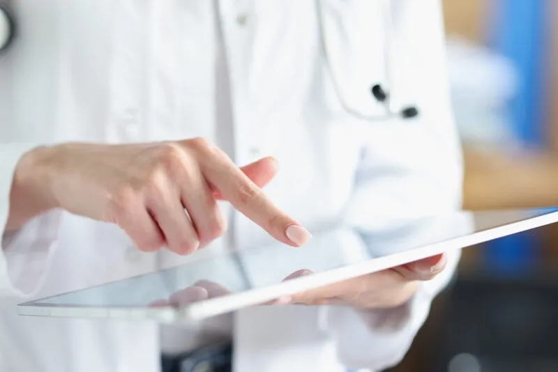 Healthcare professional in a lab coat using an iPad Mini to review patient information, provided by iPadify at wholesale prices for medical institutions, ensuring both quality and affordability.