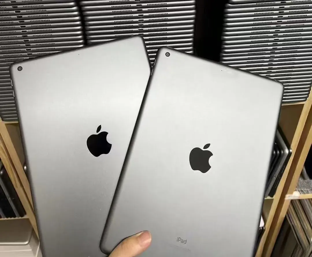 Close-up of two pristine Grade A refurbished iPads in Space Gray, held in front of neatly stacked wholesale inventory.